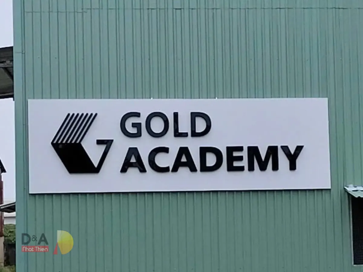 Bảng hiệu alu chữ nổi Gold Academy với logo và chữ nổi màu đen trên nền trắng tại khu vực kinh doanh.